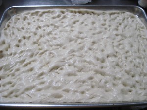 use your fingers to spread out the focaccia dough onto an oiled half sheet pan until the dough fills the entire pan